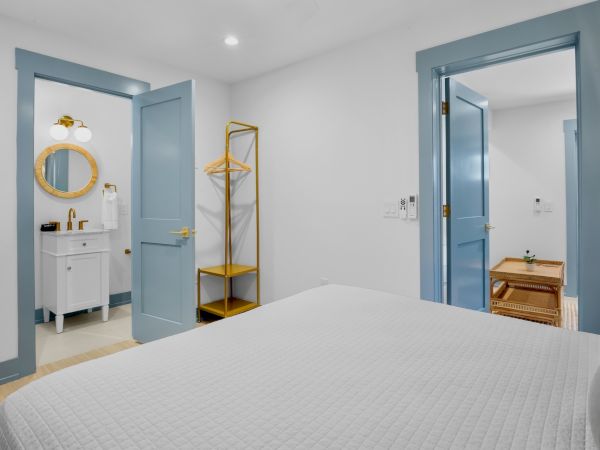 A bedroom features two doors; one leads to a bathroom with a circular mirror, the other to a room with a wooden coffee table.