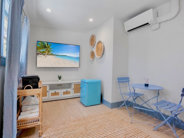 A cozy room with a TV, blue chairs, and air conditioning; decor includes wall baskets and a beach scene on the screen.