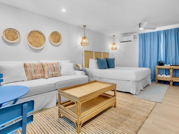 A cozy, modern room with a large bed, sofa, blue chairs, wicker elements, decorative plates on the wall, and blue curtains.