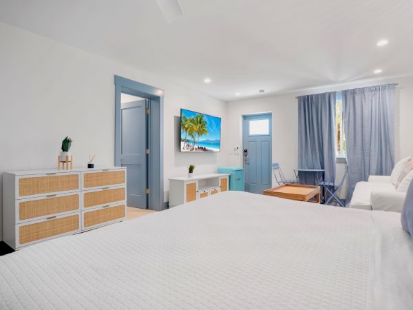 A bright bedroom with a bed, dresser, TV, sofa, blue accents, and curtains in a modern, minimalist style.