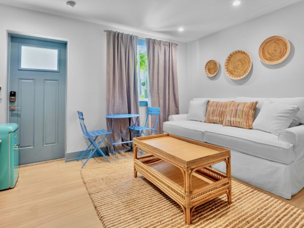 A cozy living room with a white sofa, wicker coffee table, and wall baskets. There’s a small blue table with chairs by the window.