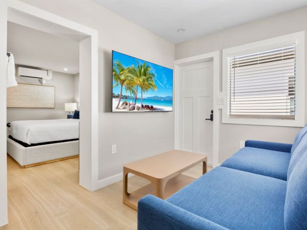 The image shows a modern living space with a blue couch, a wooden table, and a wall-mounted TV displaying a beach scene.