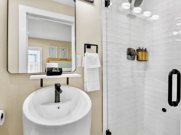 A modern bathroom with a round sink, mirror, towel rack, shower with glass door, and mounted toiletries. Minimalist and clean design.