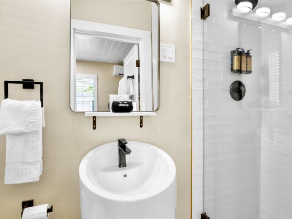 A modern bathroom with a round sink, black faucet, mirror, towel holder, and glass shower enclosure with dark fixtures and toiletries.