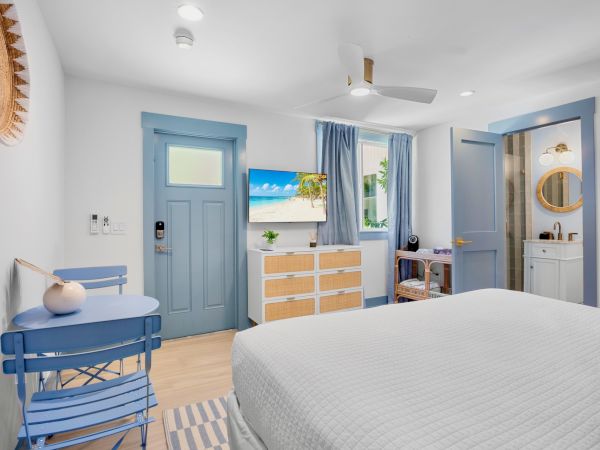 A cozy bedroom with blue accents, a bed, a TV, and a small table and chair, offering a bright and tranquil atmosphere.