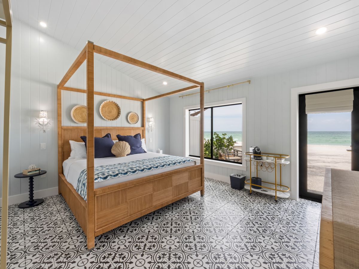 A coastal bedroom features a canopy bed, decorative rug, and ocean view through large windows, creating a serene escape.