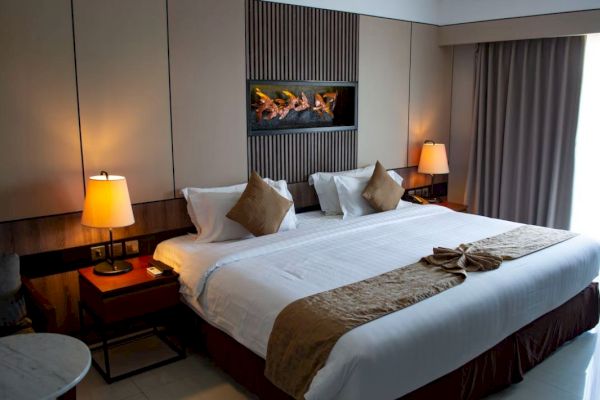 A hotel room featuring a large bed with brown accents, warm lighting from bedside lamps, and a decorative piece above.