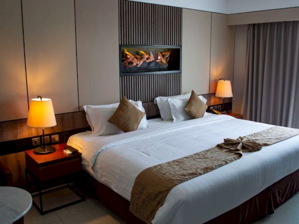 A hotel room featuring a large bed with brown accents, warm lighting from bedside lamps, and a decorative piece above.