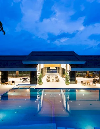 A luxurious outdoor pool area is lit up at night, with a modern building in the background under a deep blue sky.
