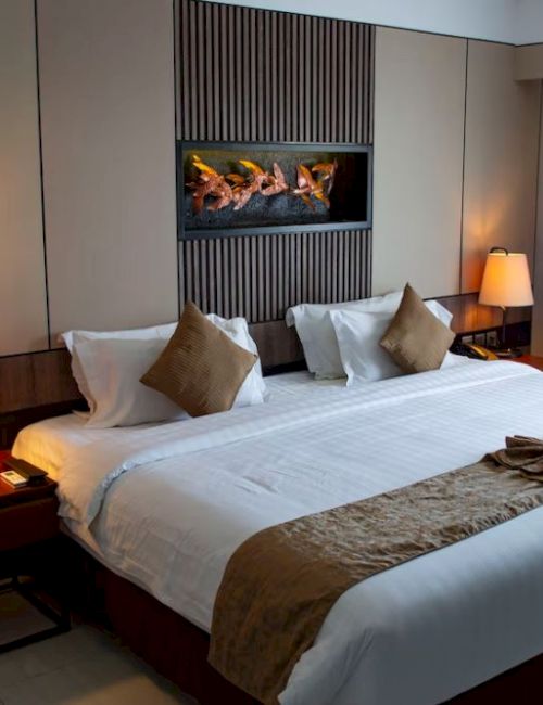 A cozy hotel room with a large bed, bedside tables with lamps, folded towels, and a decorative wall feature above the headboard.