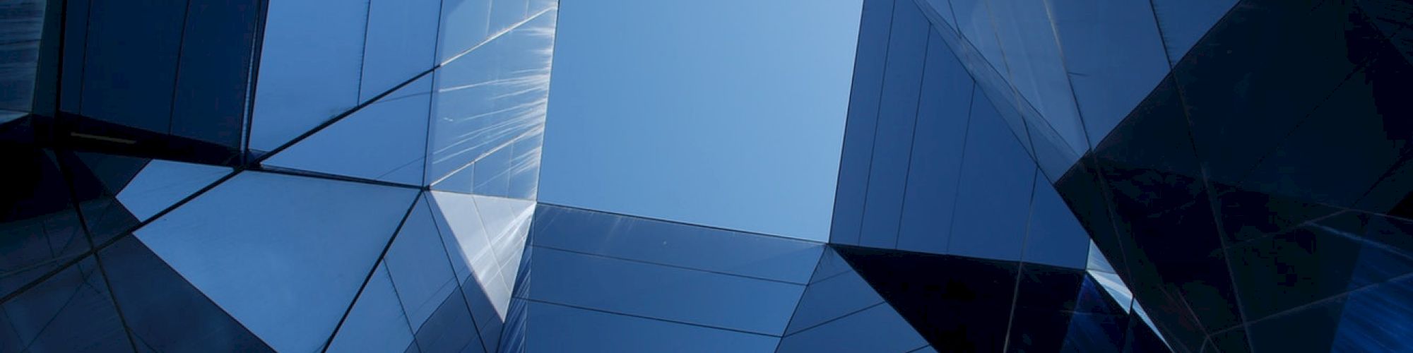 The image shows a geometric architectural structure with mirrored surfaces reflecting a blue sky in the center.