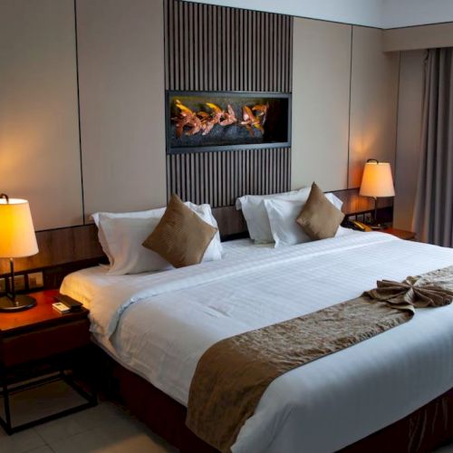 A cozy hotel room with a large bed, two bedside lamps, decorative pillows, and a window with curtains for a comfortable stay.