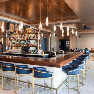 A modern bar with stools, a fully stocked back bar, chic lighting, and a seating area, creating a stylish and inviting atmosphere.