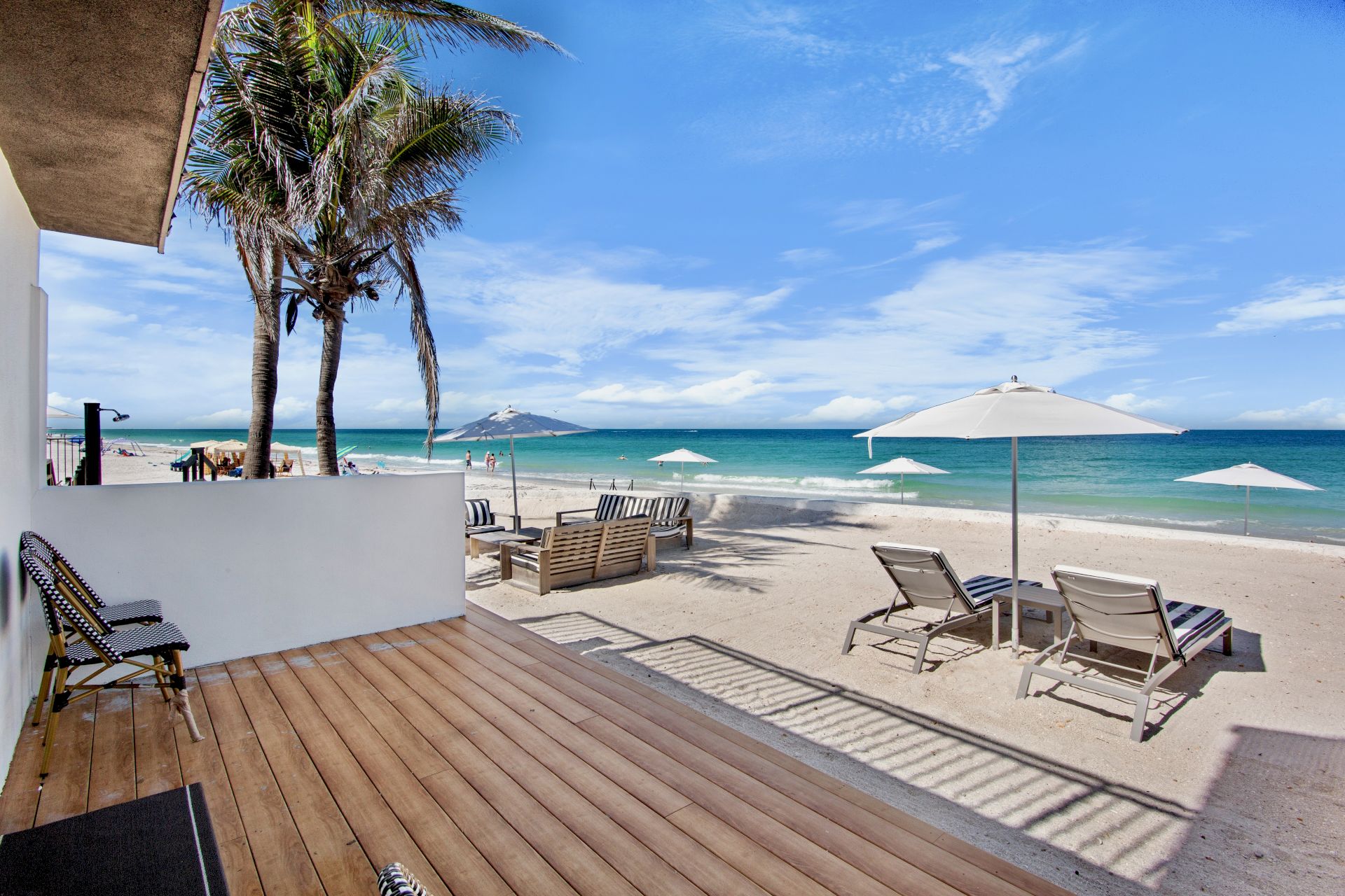 A beach scene with palm trees, lounge chairs, and umbrellas on the sand near the ocean under a clear blue sky.
