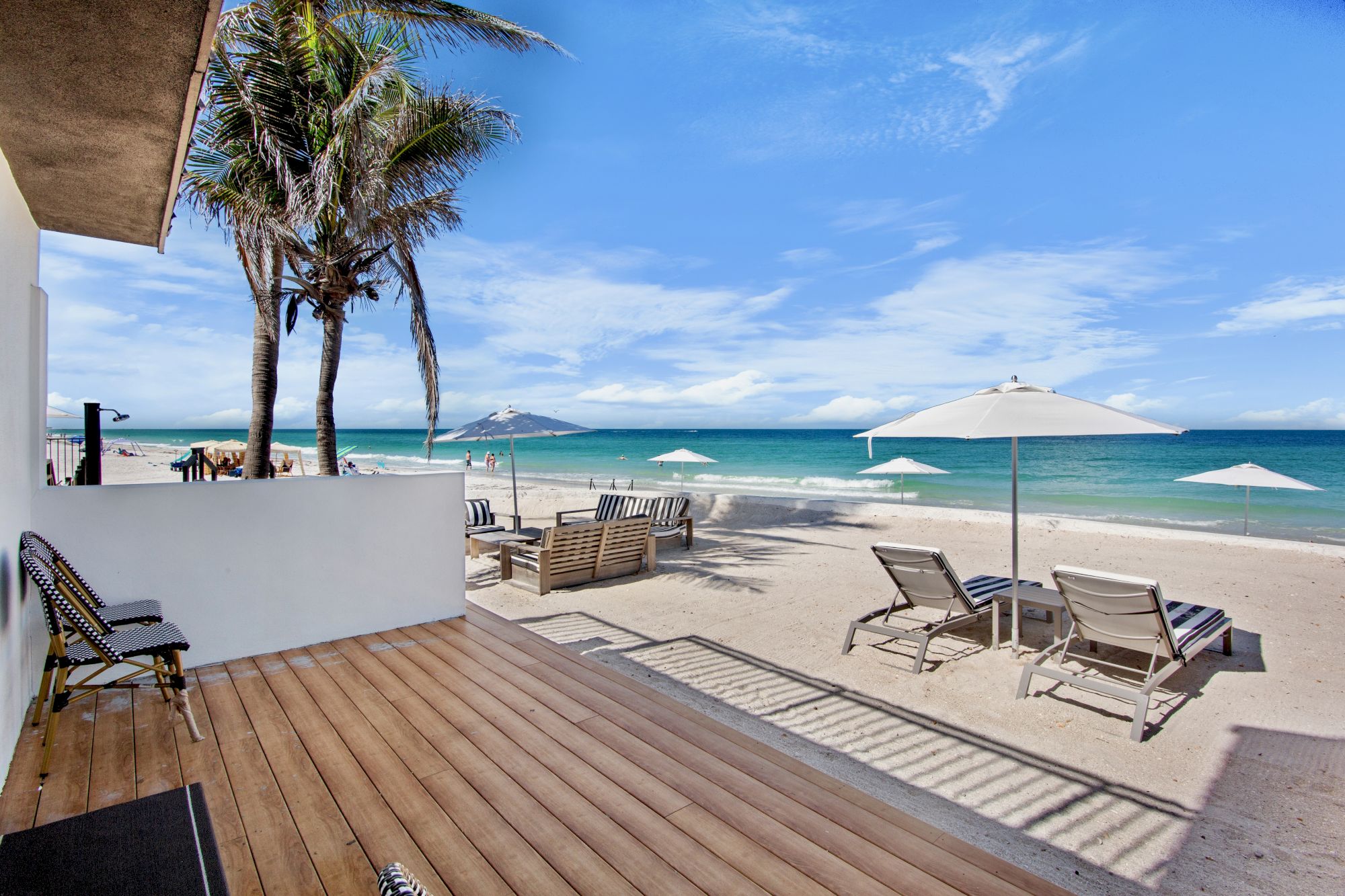 A beach scene with palm trees, lounge chairs, and umbrellas on the sand near the ocean under a clear blue sky.