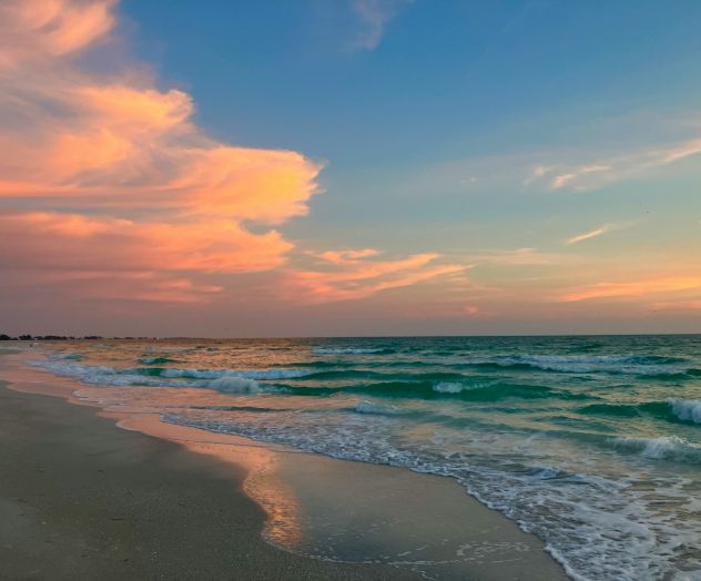 A scenic beach at sunset with vibrant pink and orange clouds, gentle waves, and a wide sandy shore.