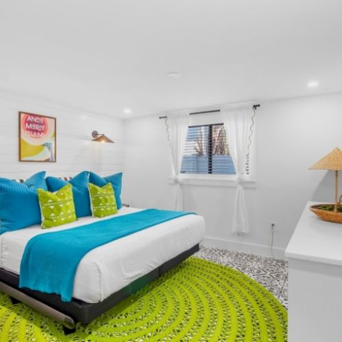 A bright bedroom with a bed, blue and green accents, a round rug, wall art, and a TV, creating a vibrant and cozy atmosphere.