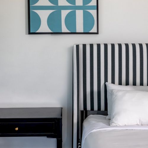 A bed with black and white striped headboard beside a black nightstand, with abstract blue and white wall art above.