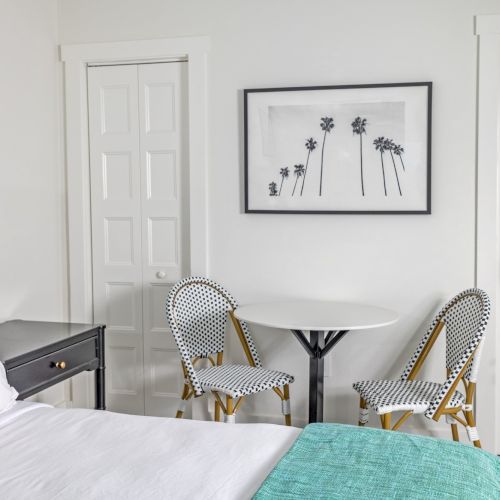 Bedroom with a bed, striped headboard, small table with chairs, palm tree artwork on the wall, and a door with a mirror.