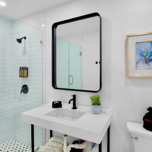 Modern bathroom with a glass shower, white sink, wall art, and decor on the toilet.
