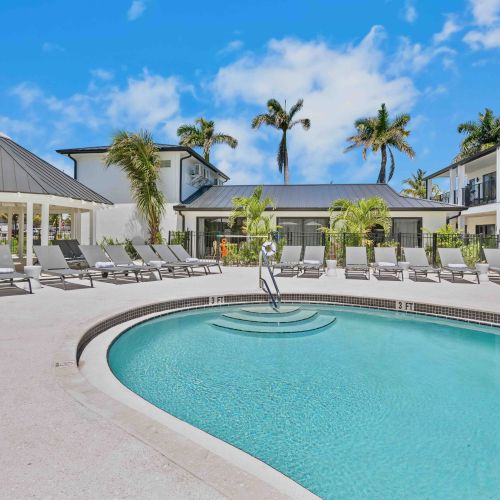 A sunny resort pool with turquoise water, palm trees, and white buildings lining the deck.