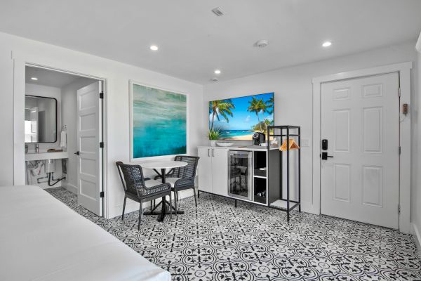 The image shows a modern room with patterned tile floors, a small dining area, a kitchenette, a bathroom, and a door.