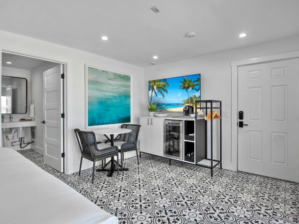 The image shows a modern room with patterned tile floors, a small dining area, a kitchenette, a bathroom, and a door.