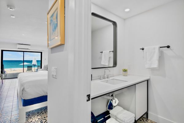 A bathroom with a large mirror and a bedroom with a beach view beyond a glass door.