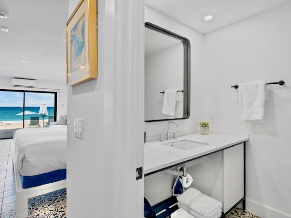A bathroom with a large mirror and a bedroom with a beach view beyond a glass door.