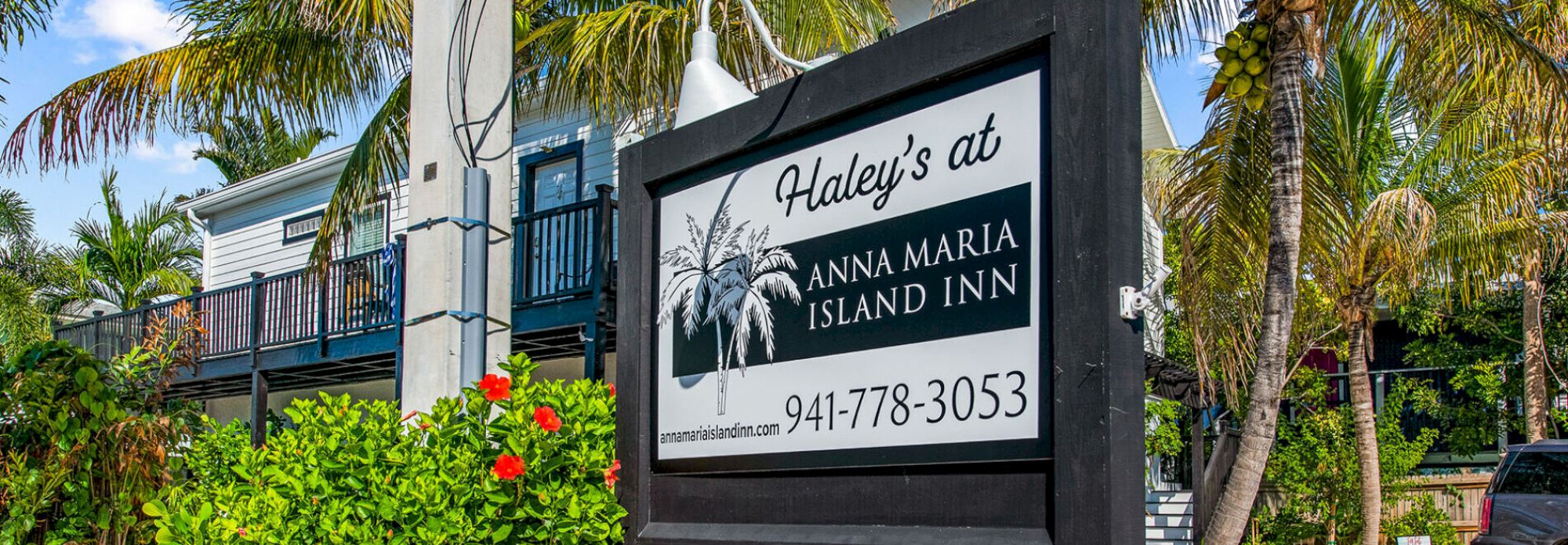 A sign for Haley's at Anna Maria Island Inn surrounded by palm trees and greenery.