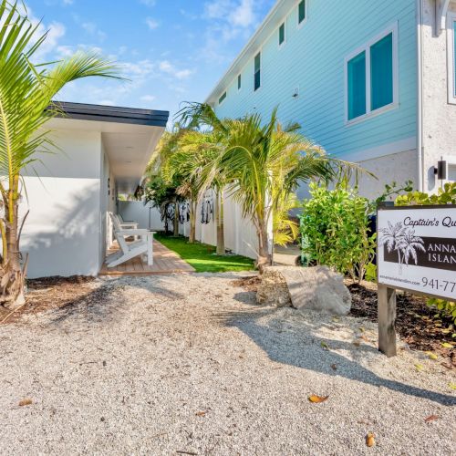 A pathway with tropical plants leads to buildings. A sign reads "Anna Maria Island Inn" with a phone number.