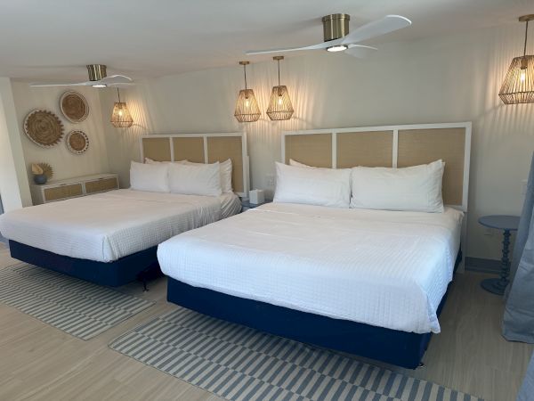 The image shows a bedroom with two beds, white bedding, decorative wall baskets, and hanging lamps, creating a cozy ambiance.