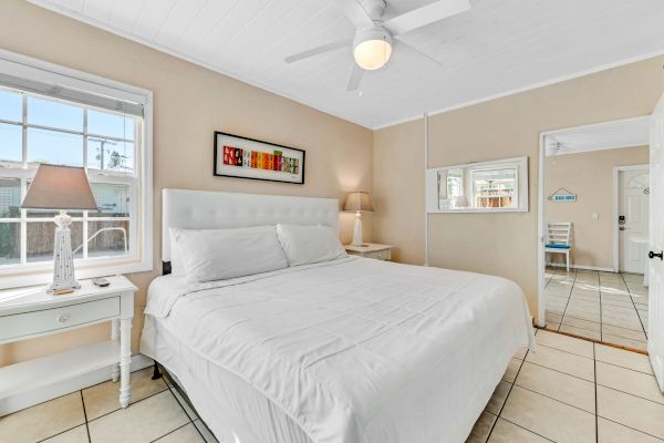 A cozy bedroom features a large bed, two side tables with lamps, a ceiling fan, and a window, creating a bright and inviting space.