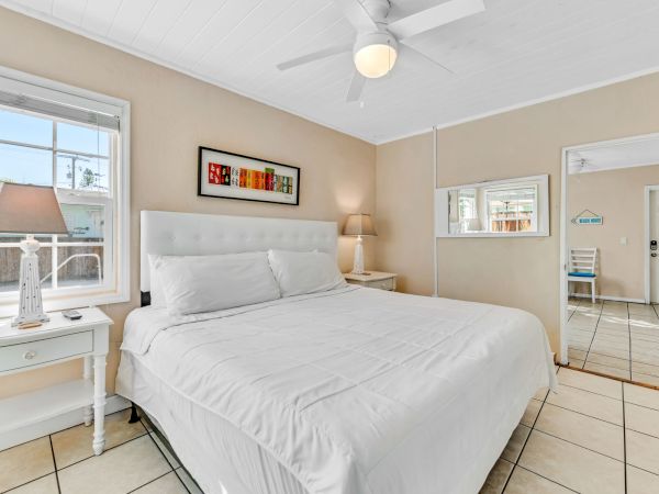 A cozy bedroom features a large bed, two side tables with lamps, a ceiling fan, and a window, creating a bright and inviting space.