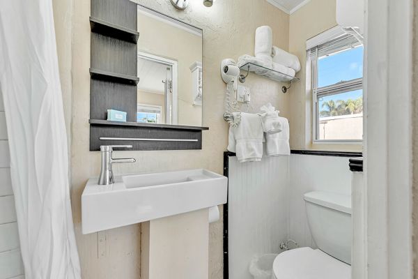 A small bathroom with a sink, mirror, hairdryer, towel racks, and a window.