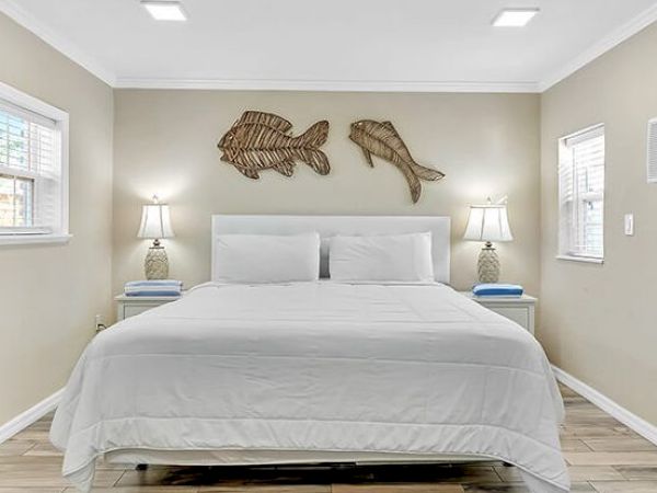 A bedroom with a large bed, two lamps on nightstands, and decorative fish wall art. The room has neutral tones and wood flooring.