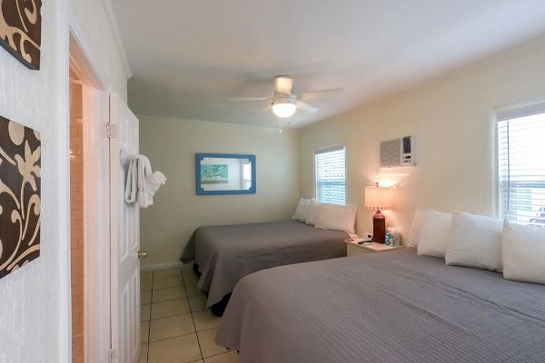A tidy bedroom with two beds, a ceiling fan, wall art, and a small bathroom visible to the left.