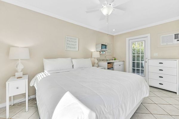A cozy bedroom with a large bed, nightstands with lamps, a dresser, and a windowed door leading outside.