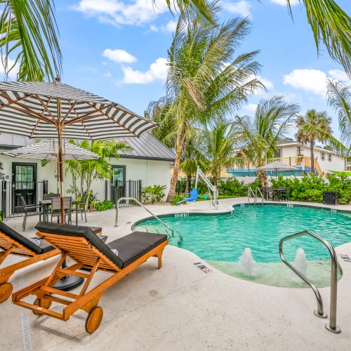 A tropical pool area with loungers, umbrellas, and lush greenery, creating a relaxing atmosphere under a blue sky.