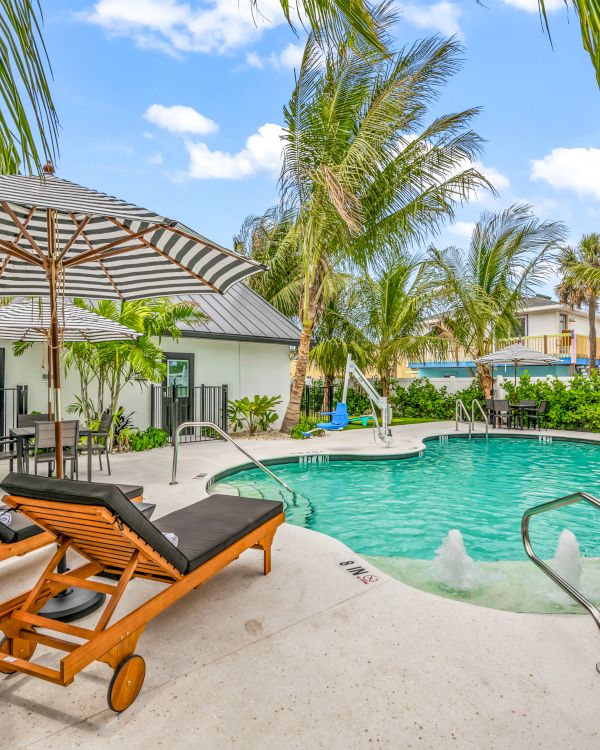 A tropical pool area with loungers, umbrellas, and lush greenery, creating a relaxing atmosphere under a blue sky.