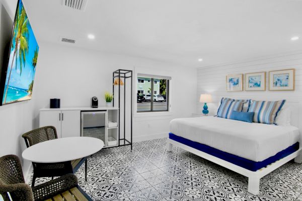 A bright room with a bed, patterned floor, table, chairs, TV, mini-fridge, and decor. It has a modern and inviting atmosphere.