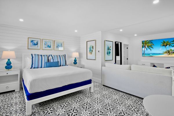 A bright, modern bedroom with patterned tile flooring, white furniture, blue accents, and tropical artwork.