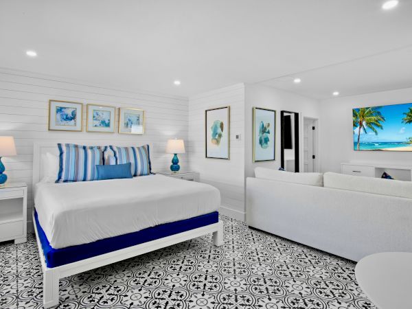 A bright, modern bedroom with patterned tile flooring, white furniture, blue accents, and tropical artwork.