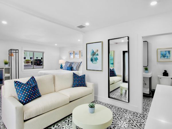 A modern living room with a white sofa, blue-patterned pillows, art on the walls, a mirror, and a small round table with a plant on top.