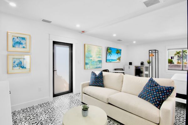 A bright living room with a beige sofa, patterned pillows, coastal artwork, a TV, and a small plant on a round table.