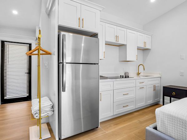 A compact, modern kitchenette with white cabinets, stainless fridge, small sink, and a wardrobe rack in a bright, minimal space.