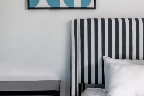 A bedroom with a black nightstand, striped headboard, white bedding, and a geometric blue and white artwork on the wall.