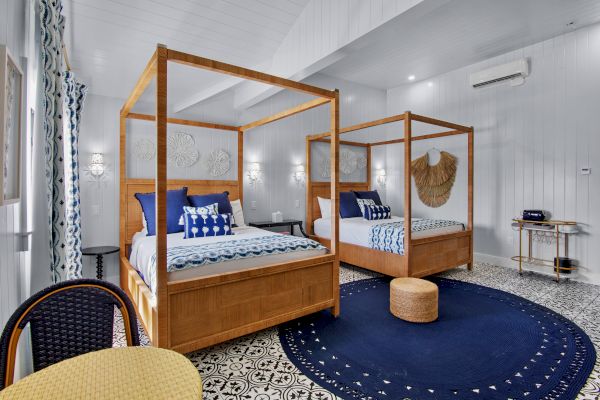 The image shows a modern bedroom with two canopy beds, blue and white decor, a woven wall piece, a round rug, and patterned flooring.