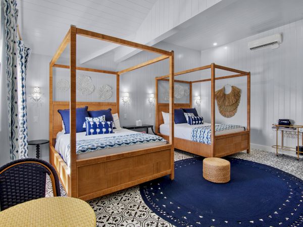 The image shows a modern bedroom with two canopy beds, blue and white decor, a woven wall piece, a round rug, and patterned flooring.