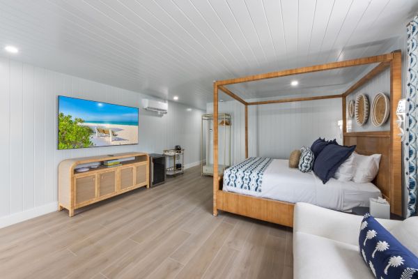 A modern bedroom with a four-poster bed, wall-mounted TV, wooden furniture, and beach-inspired decor in a bright, spacious setting.